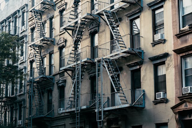 Row of New York City apartment buildings featuring metal fire escapes on their exterior facades.