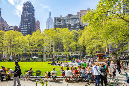 Spring in New York City with people enjoying Bryant Park as trees bloom and Midtown skyline rises in the background